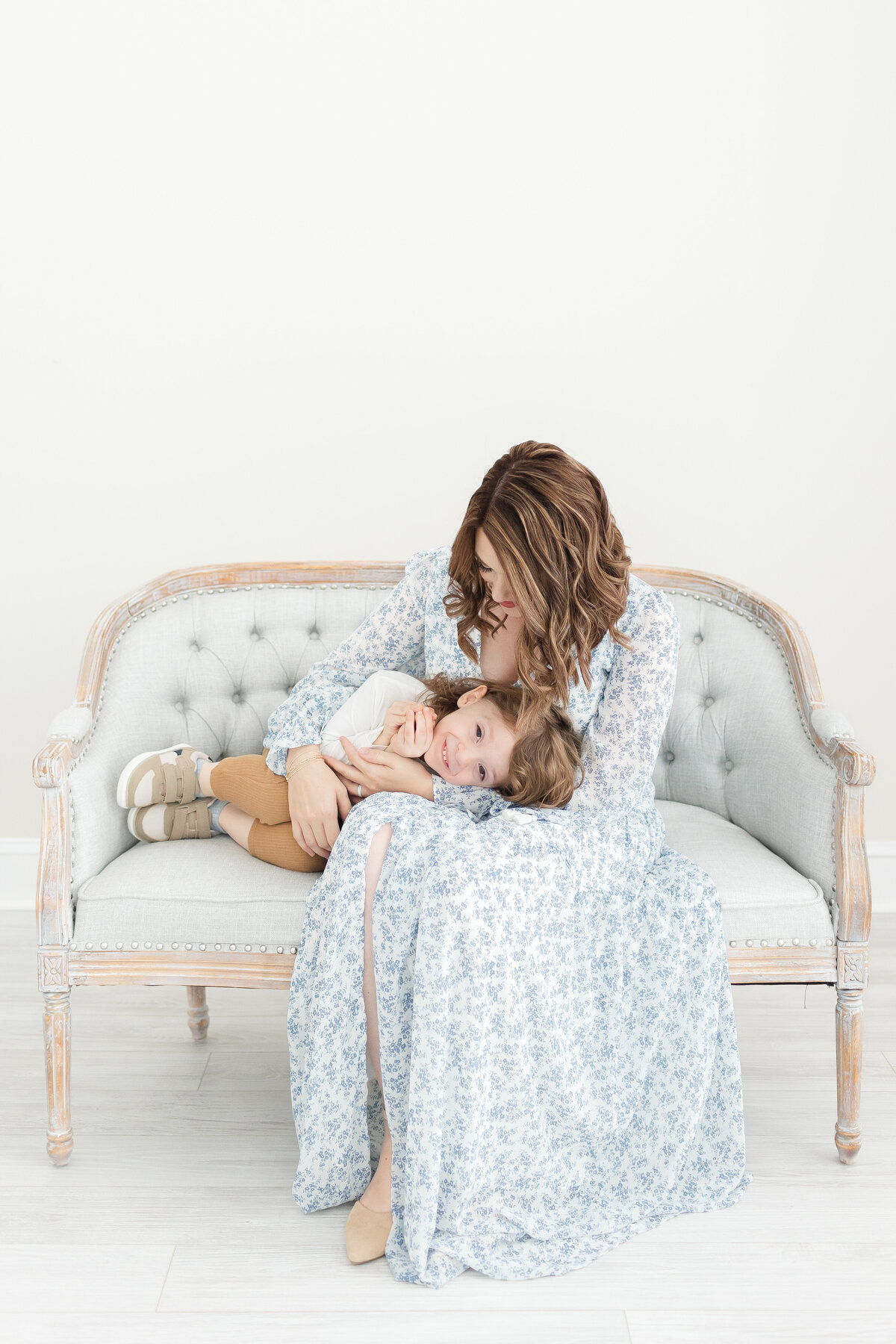 A mother snuggling with her young son on a bench wearing a blue dress in our Northern Virginia Newborn Photography studio