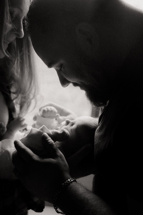 Père et mère contemplant leur bébé. Photo en noir et blanc. Shooting photo naissance par Kamescop.