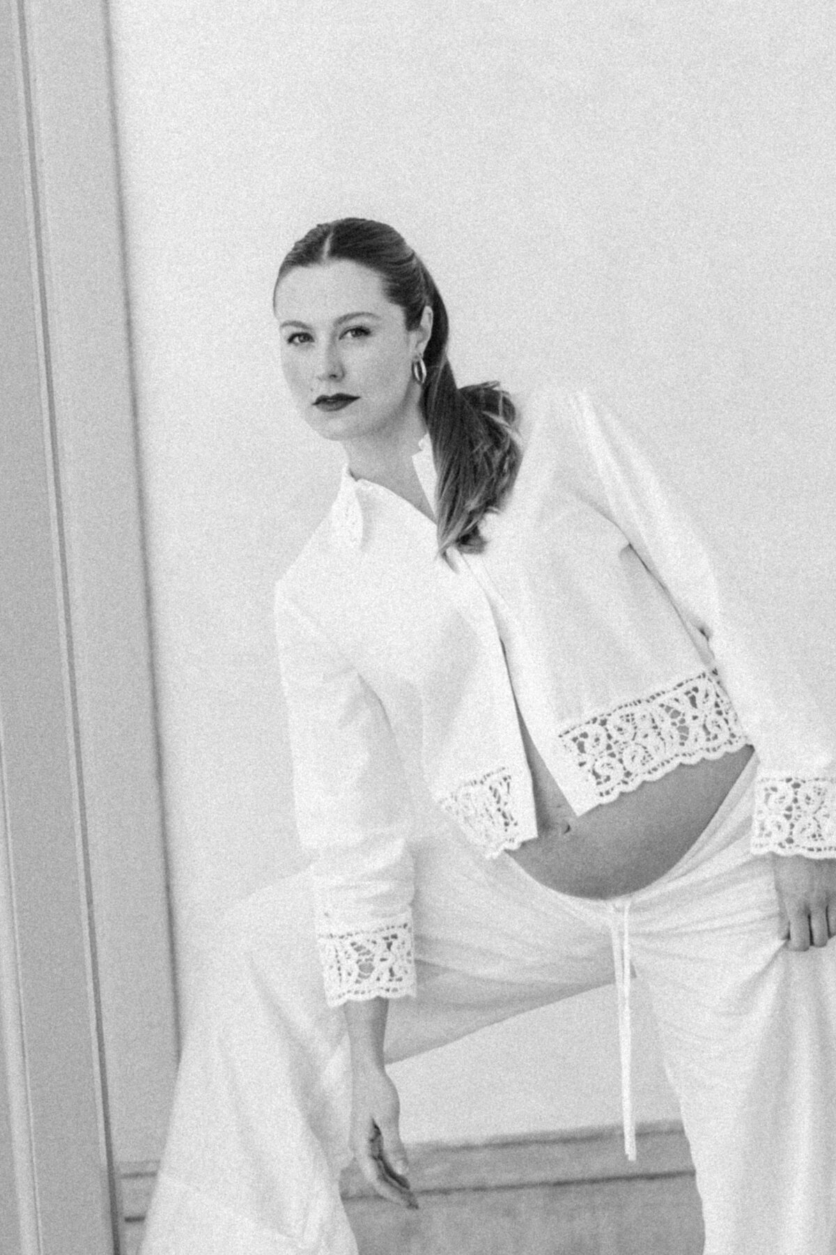 Editorial black-and-white maternity portrait of a poised mother-to-be in heels, framed by architectural columns