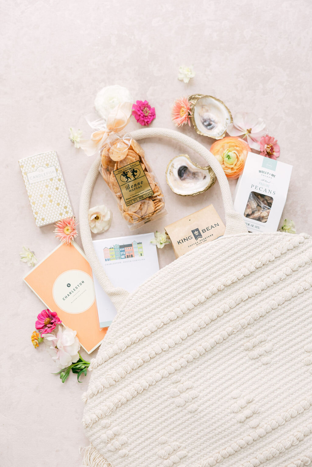 Flat-lay of a woven white tote filled with Charleston treats—pecans, coffee, oyster-shell dishes, and local guides—welcome bag detail for a Dewberry Hotel wedding, captured by luxury wedding photographer Amia Marcell.