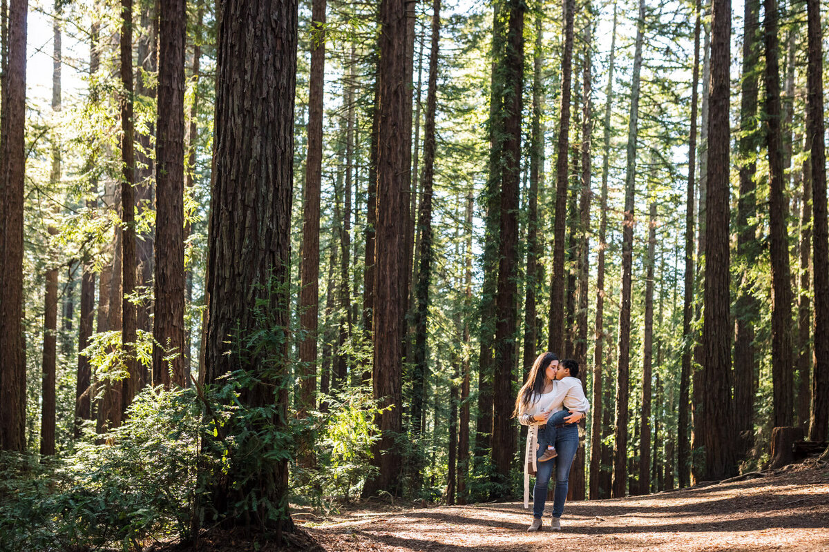 mom holding and snuggling 4-year-old son while standing among Oakland redwood trees