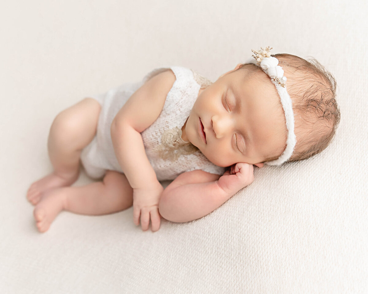 baby girl with white headband laying on side in baby photos
