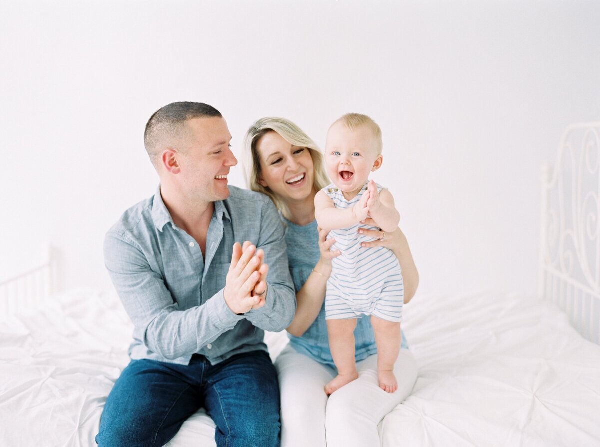 candid photo of Seattle family with toddler boy clapping and smiling in all white studio 
