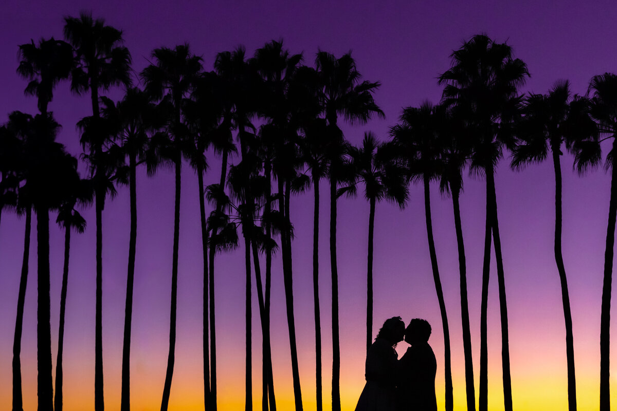 Silhouette of a couple kissing with a purple sky behind them.