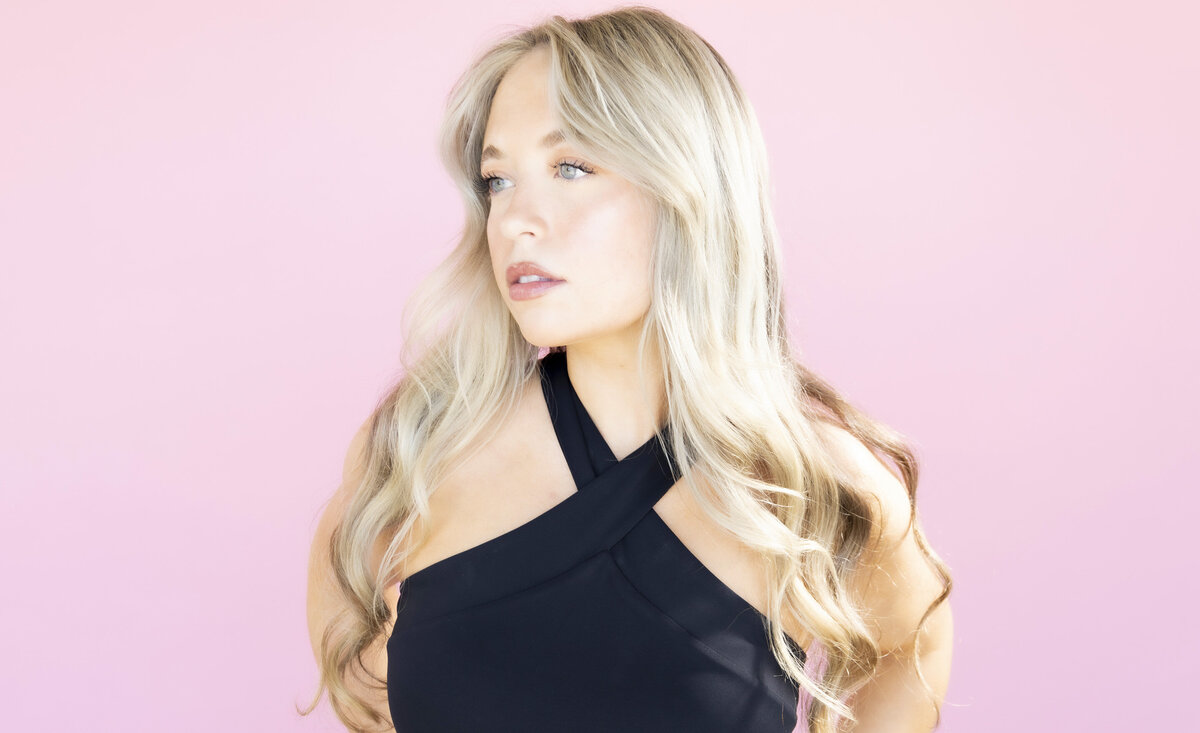 Female musician portrait Chloe DeMore wearing black tank top against pink backdrop
