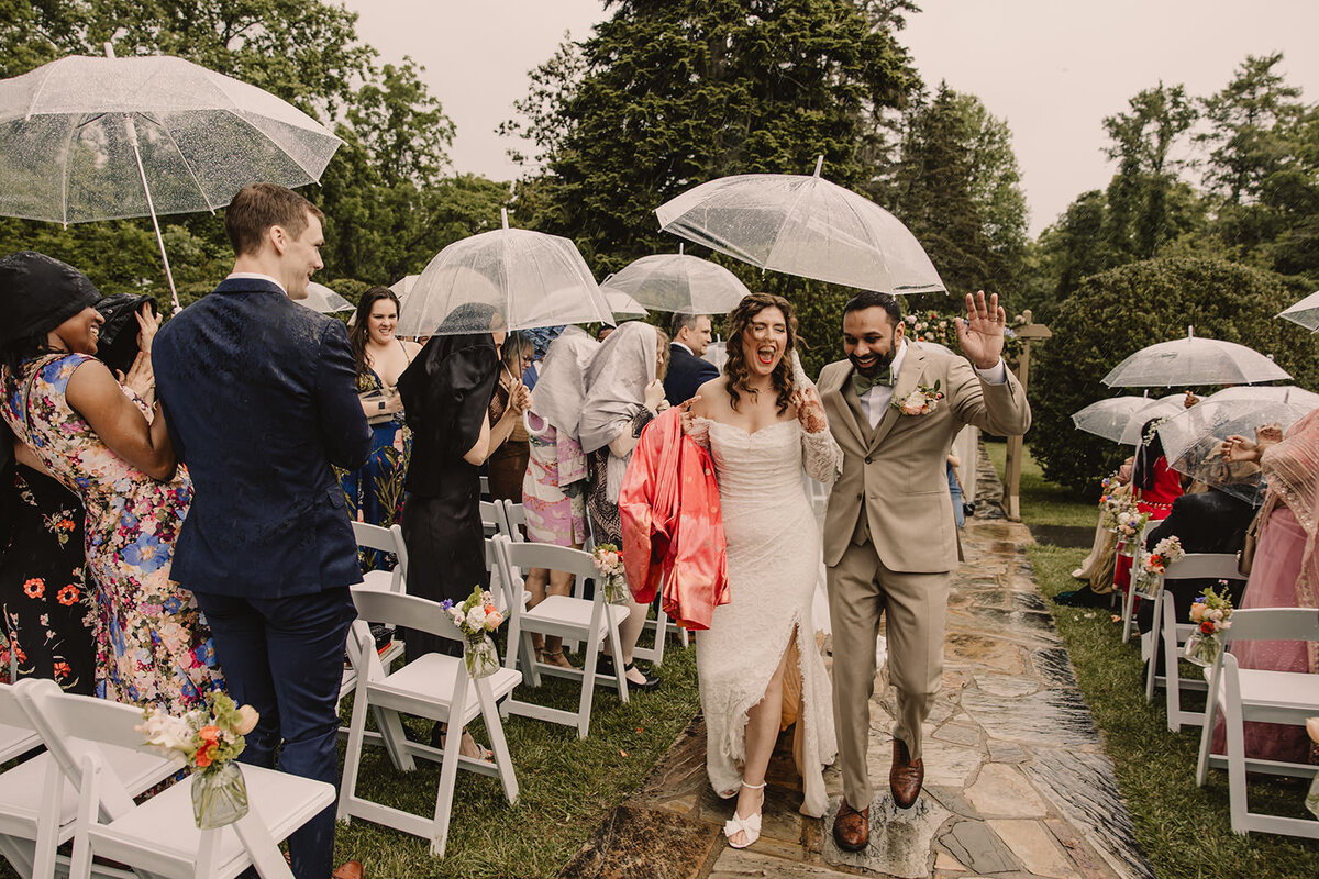 Newlyweds walking back up the aisle while holding a clear umbrella 