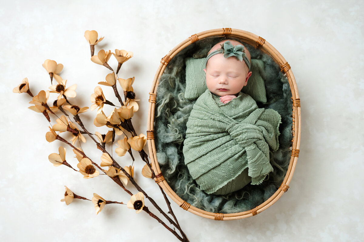 Embrace the beauty of nature with a newborn baby girl, nestled in a green basket with soft floral accents. A timeless photo captured by our Pittsburgh newborn photographer.