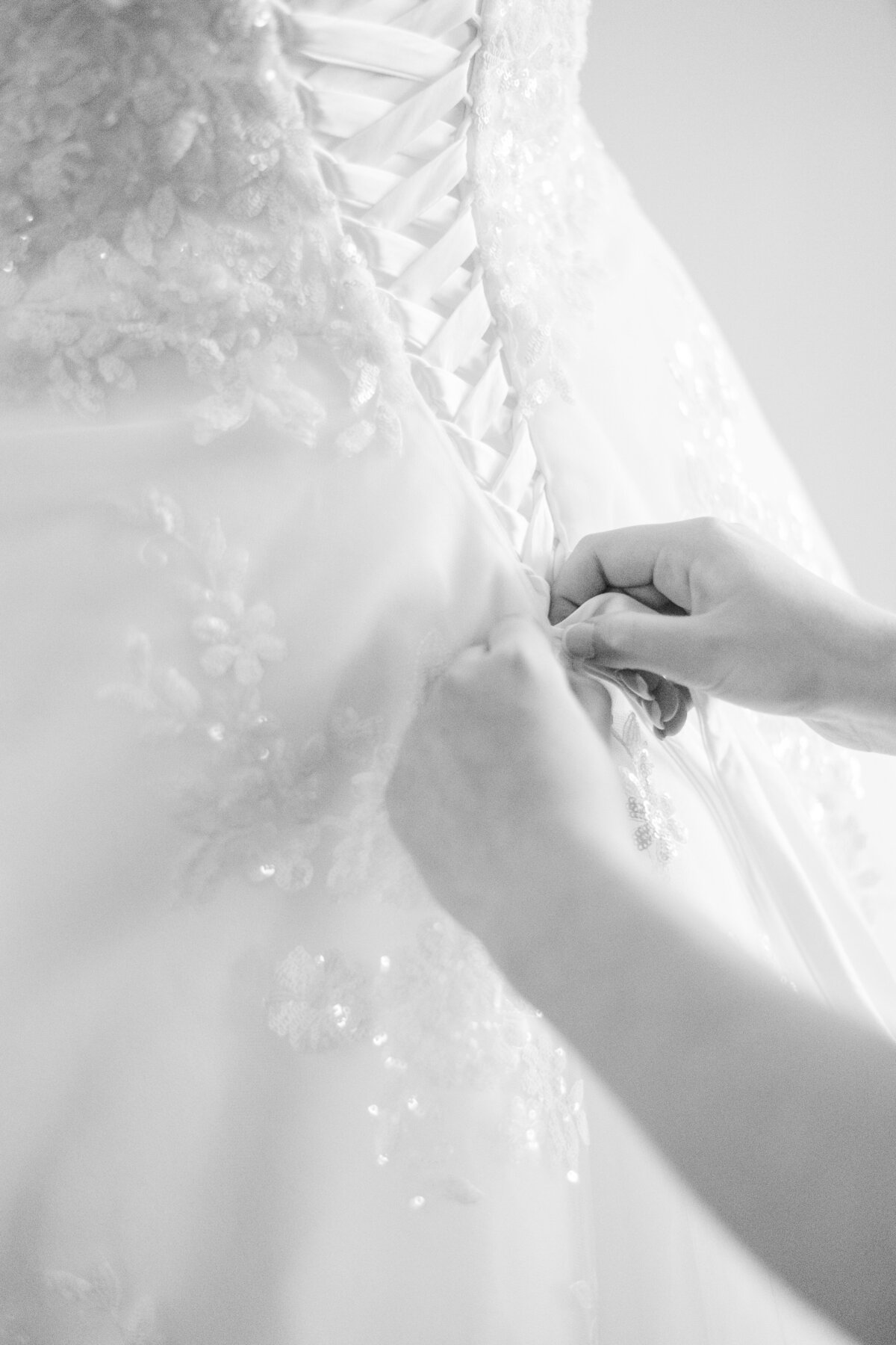 Photo of someone helping the bride lace up her elaborate wedding dress in black and white