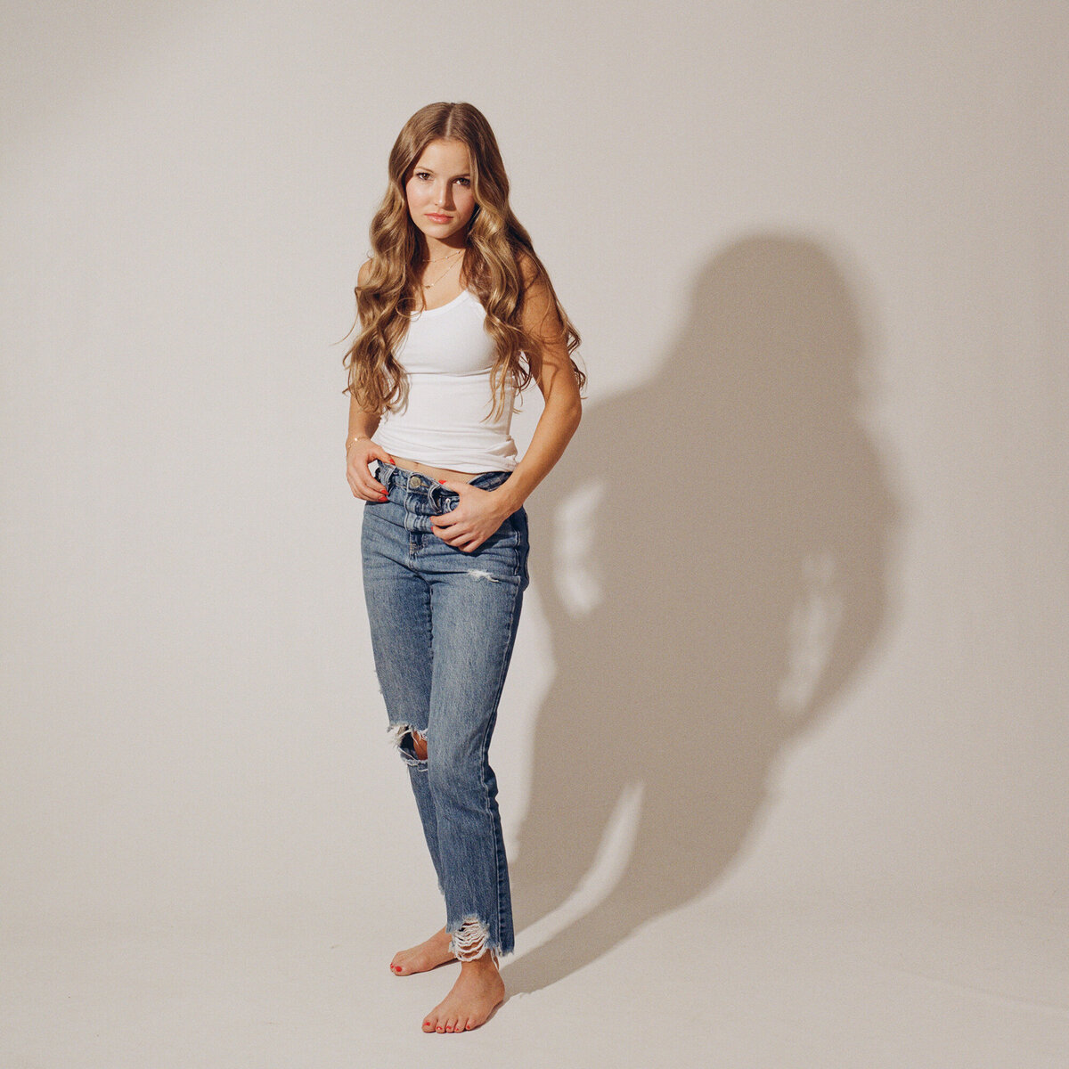 A high school grad stands in a studio with hands in her pockets