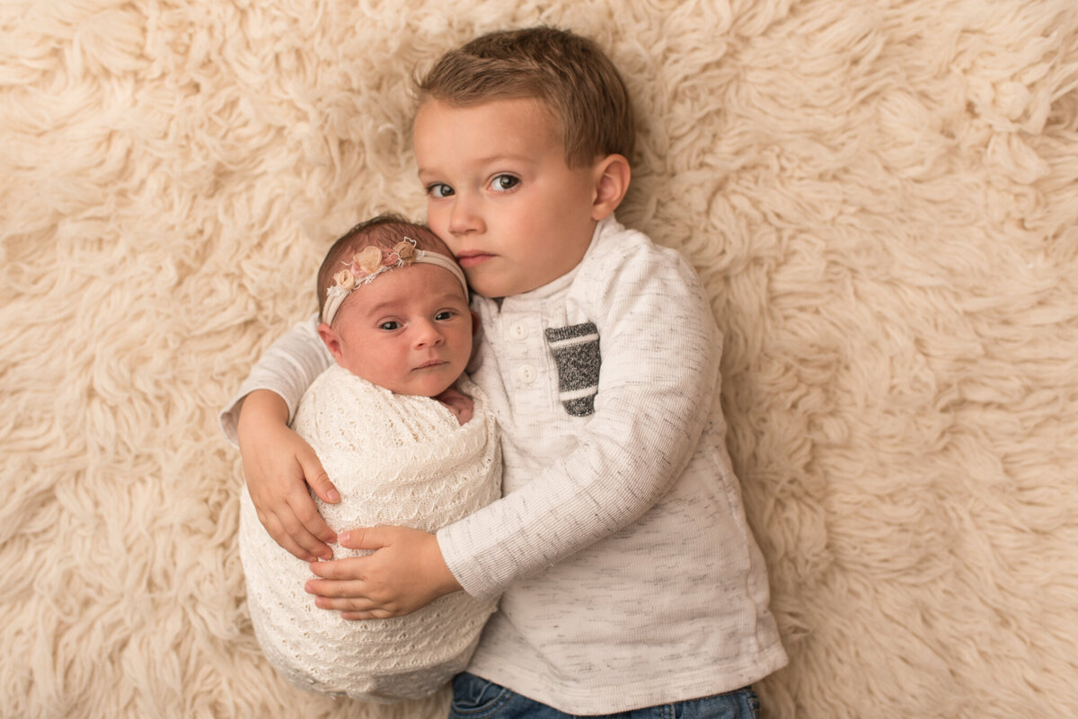 Brother laying on fur, holding baby sister