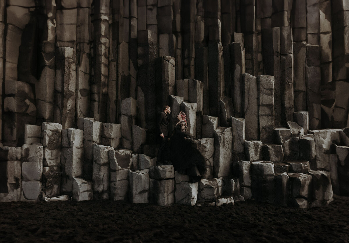 A bride wearing a black wedding dress and her groom standing on pillars at the famous black beach in Iceland.