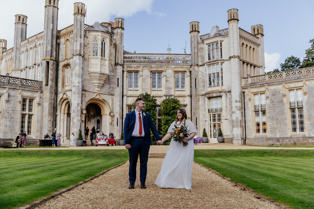 Bride and groom hold hands looking at eachother infront of Highcliffe Castle