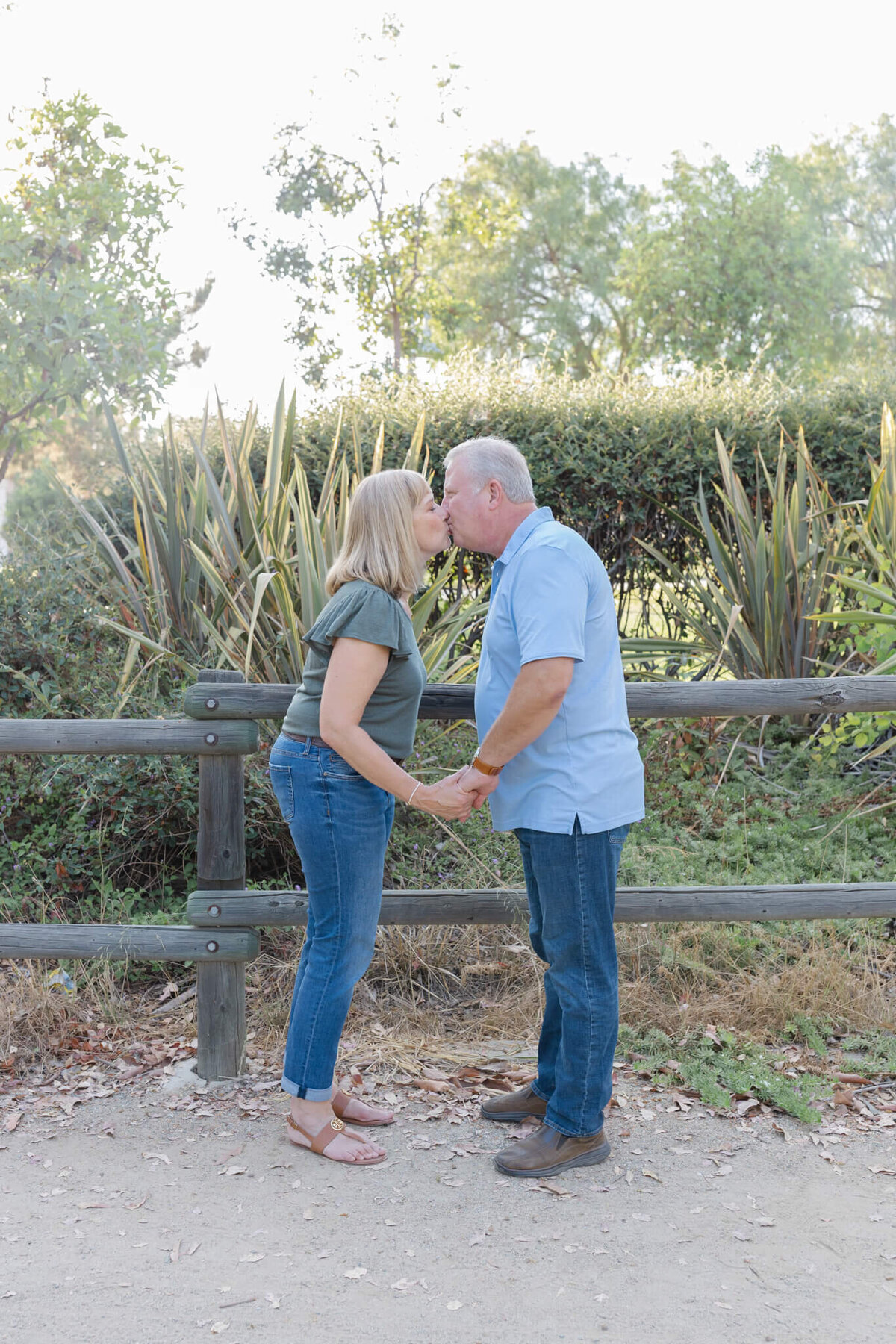 A husband and wife with blonde hair facing each other and kissing while holding hands.