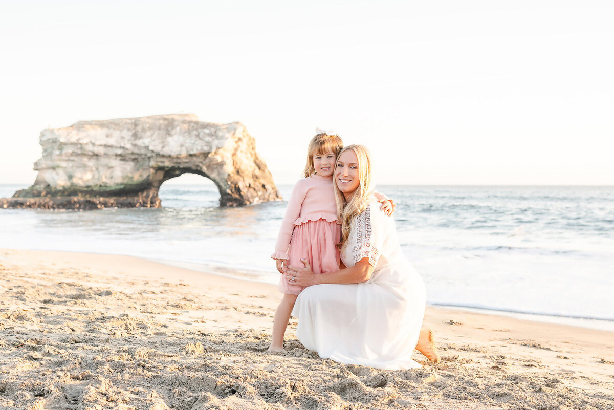 mother and daughter at Natural Bridges Beach with the rock formation behind them