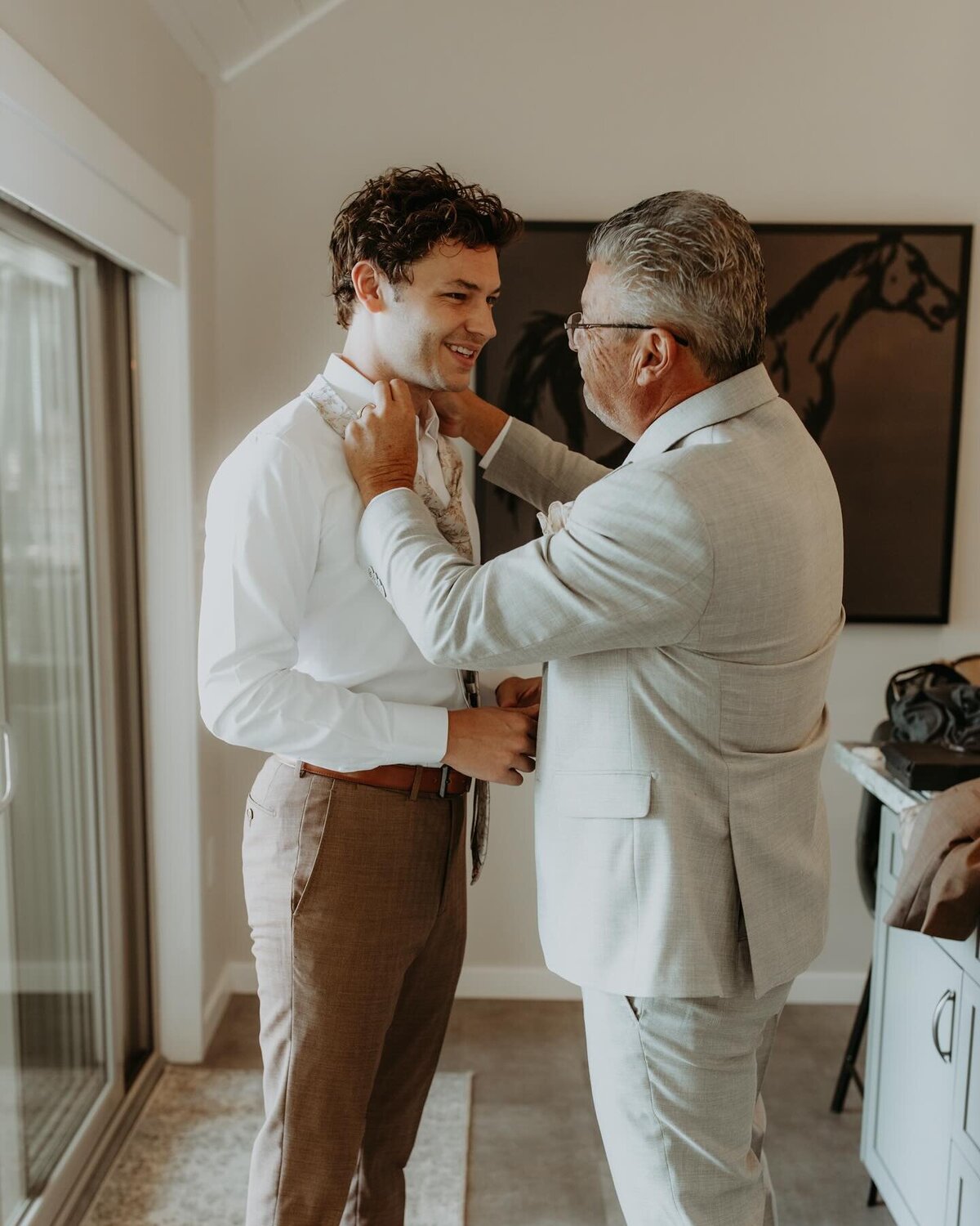 A father wearing a heathered suit straightens his son’s tie