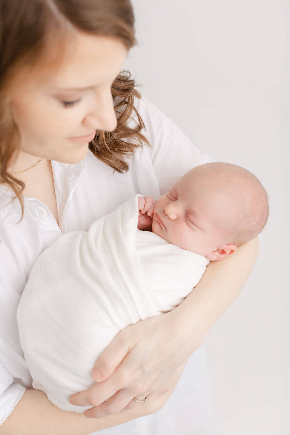 Mom in white shirt holding her baby who is swaddled in white during newborn photos.