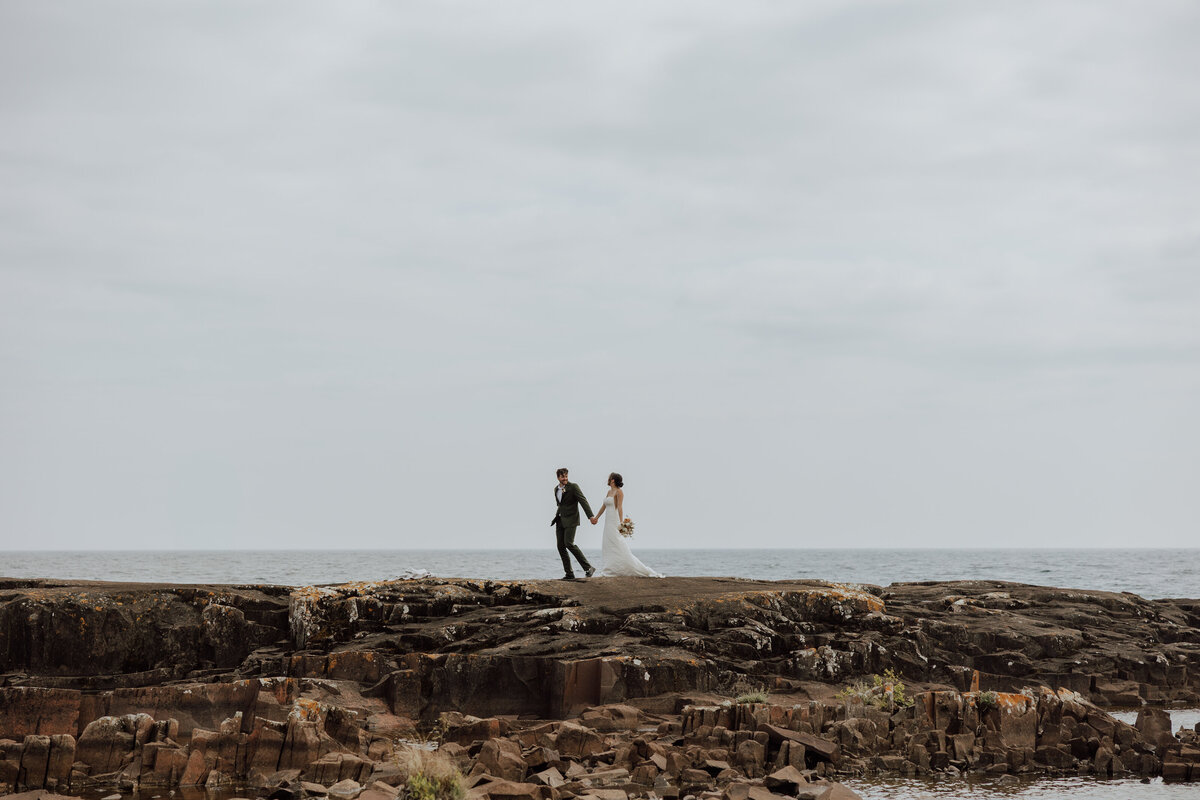 elopement on the north shore of minnesota. couple is walking along a rocky area on lake superior