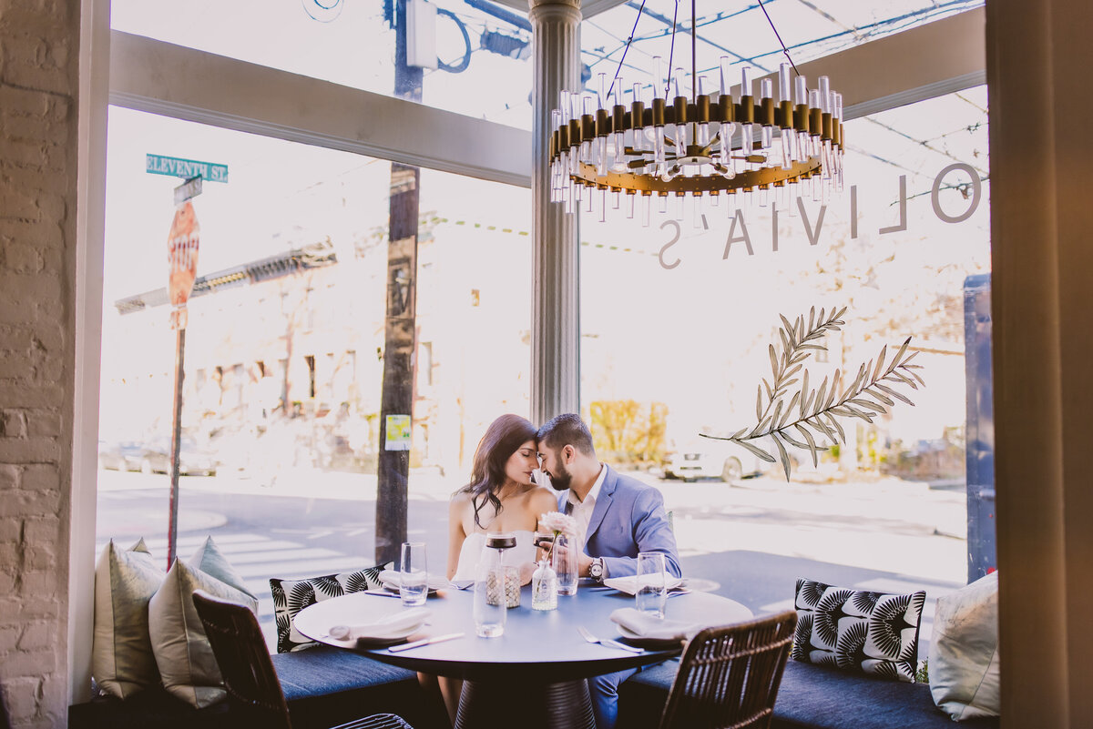 an engaged couple sharing a moment sitting in the corner of a restaurant with panoramic windows called Olivia's in Hoboken with espresso martinis