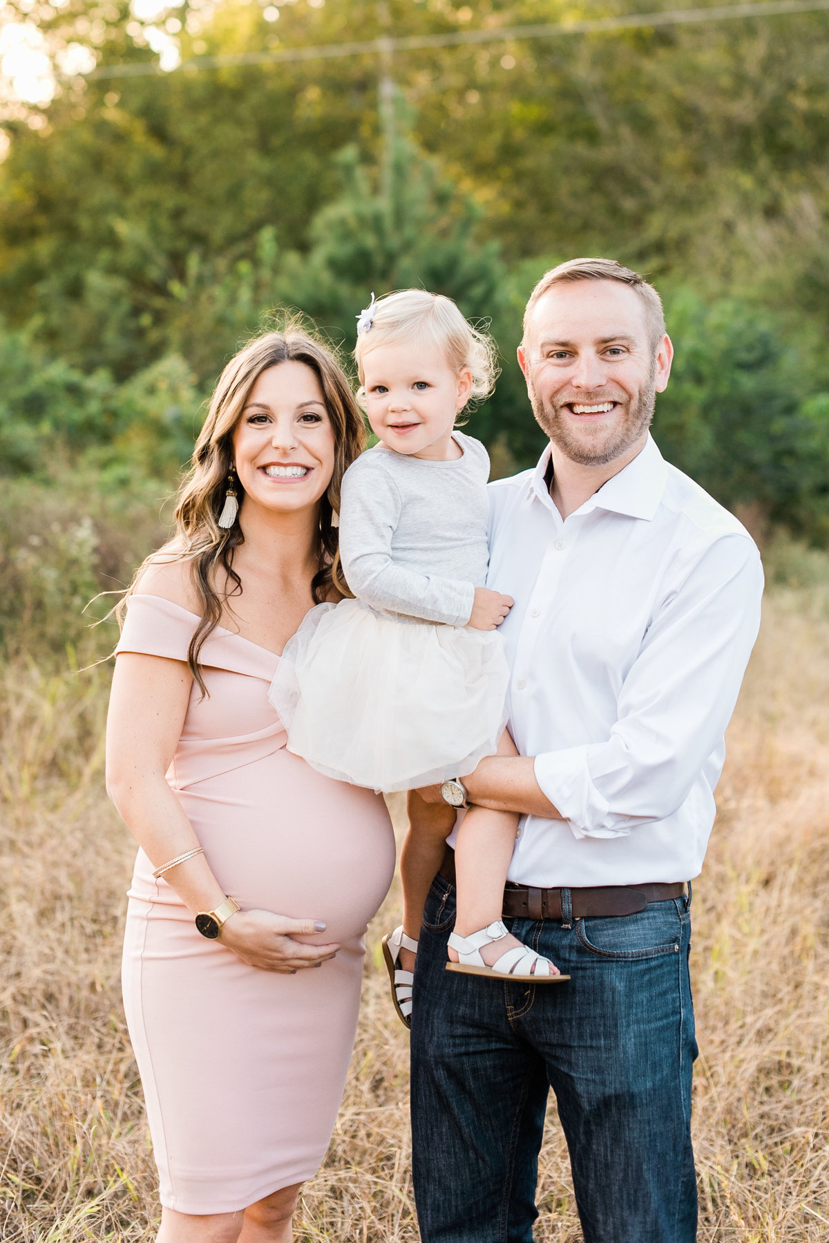 Family smiles at the camera during a maternity photo session in Raleigh NC. Photographed by Raleigh Maternity Photographer A.J. Dunlap Photography.