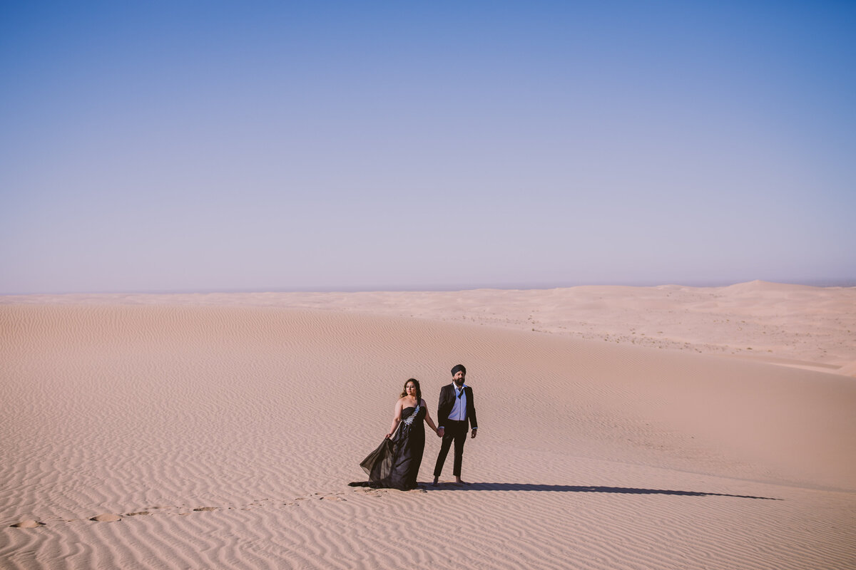 A couple standing in formal black clothing at the glamis sand dunes in san diego during their engagement session