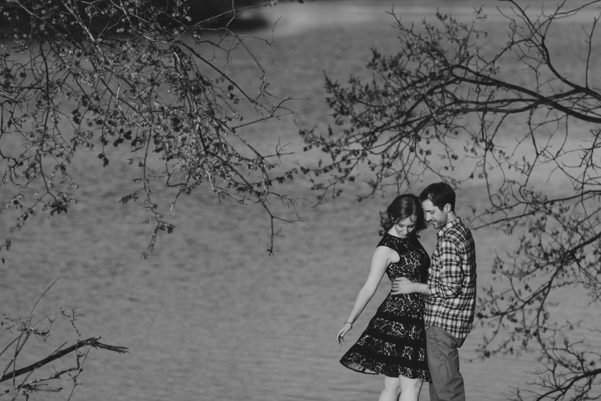 couple standing by the water surrounded by trees with dress blowing in the wind