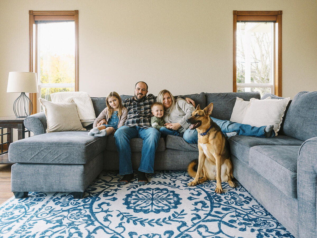 A family sitting on their couch at home with their dog sitting beside them.