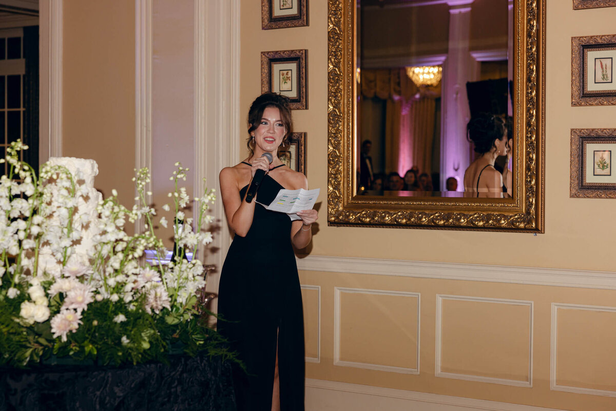 A wedding photo of the brides sister giving a speech at the reception