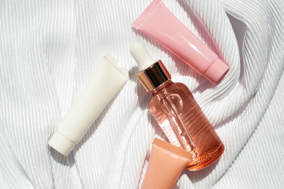 assorted pink, white and peach bottles of skincare laying on a towel in the sun