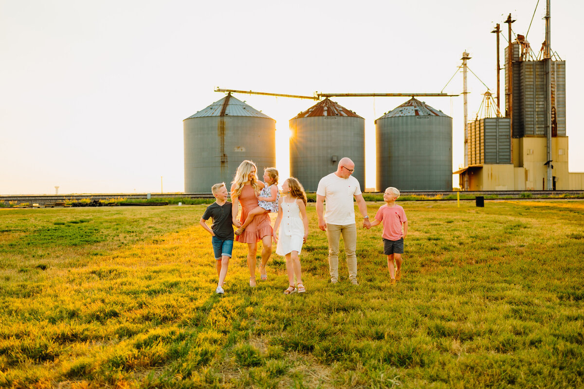 A family with four kids are posing for a mini professional photo session. They are walking on the green glass and they are dressed with vintage outfits in plano,texas