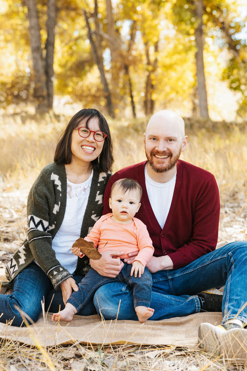 Two parents sitting in the grass with a baby sitting in between them.