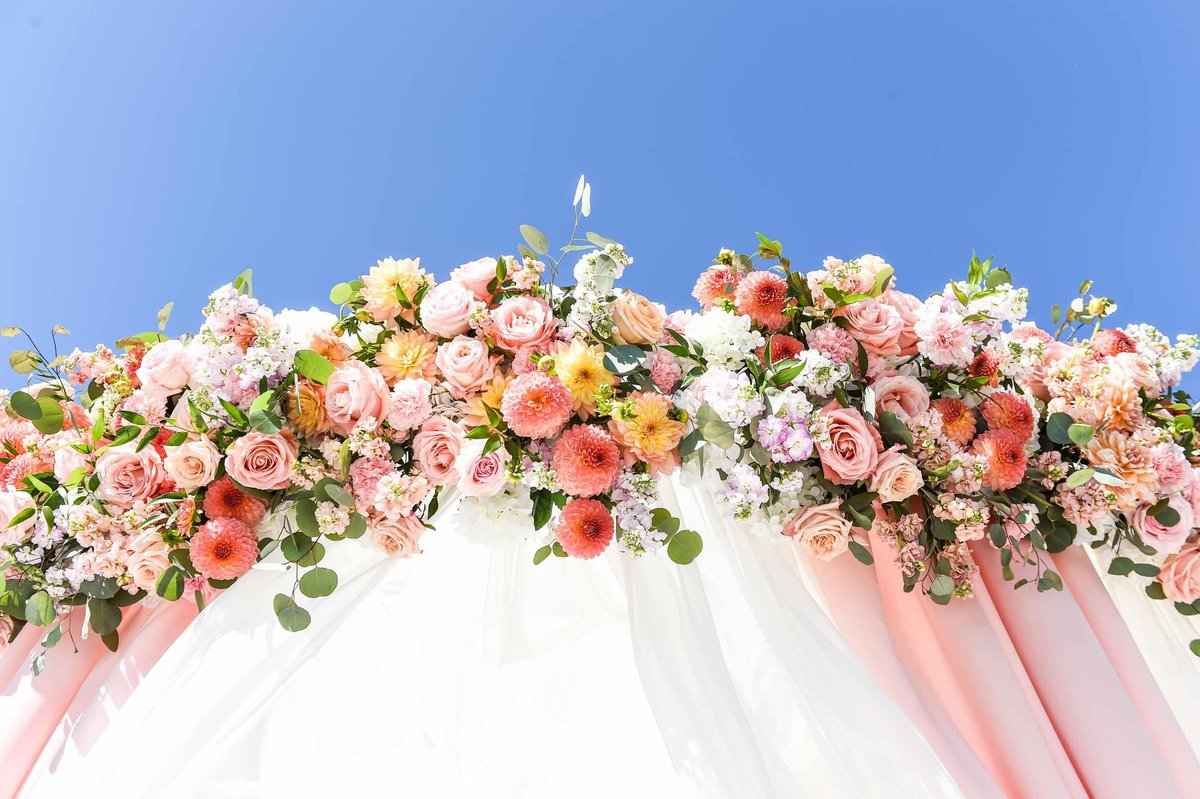 The  mandap  flowers of peach and blush roses, dahlias and stock look stunning against the blue sky at this outdoor wedding ceremony.