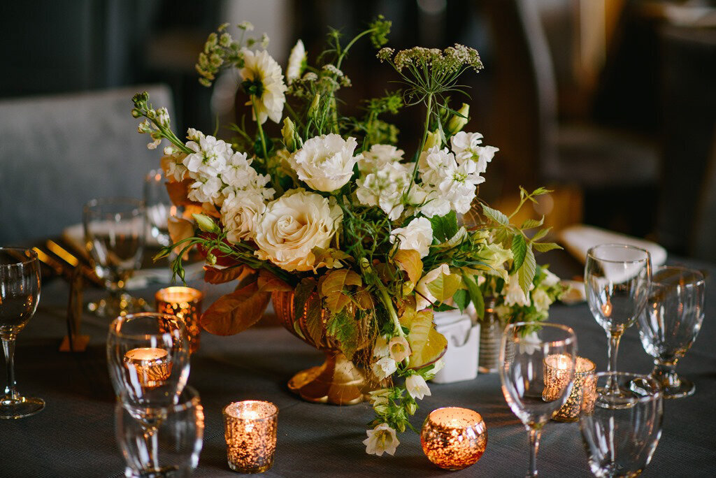 A centerpiece of white roses and greenery in a gold vase decorates a Montreal wedding reception. 