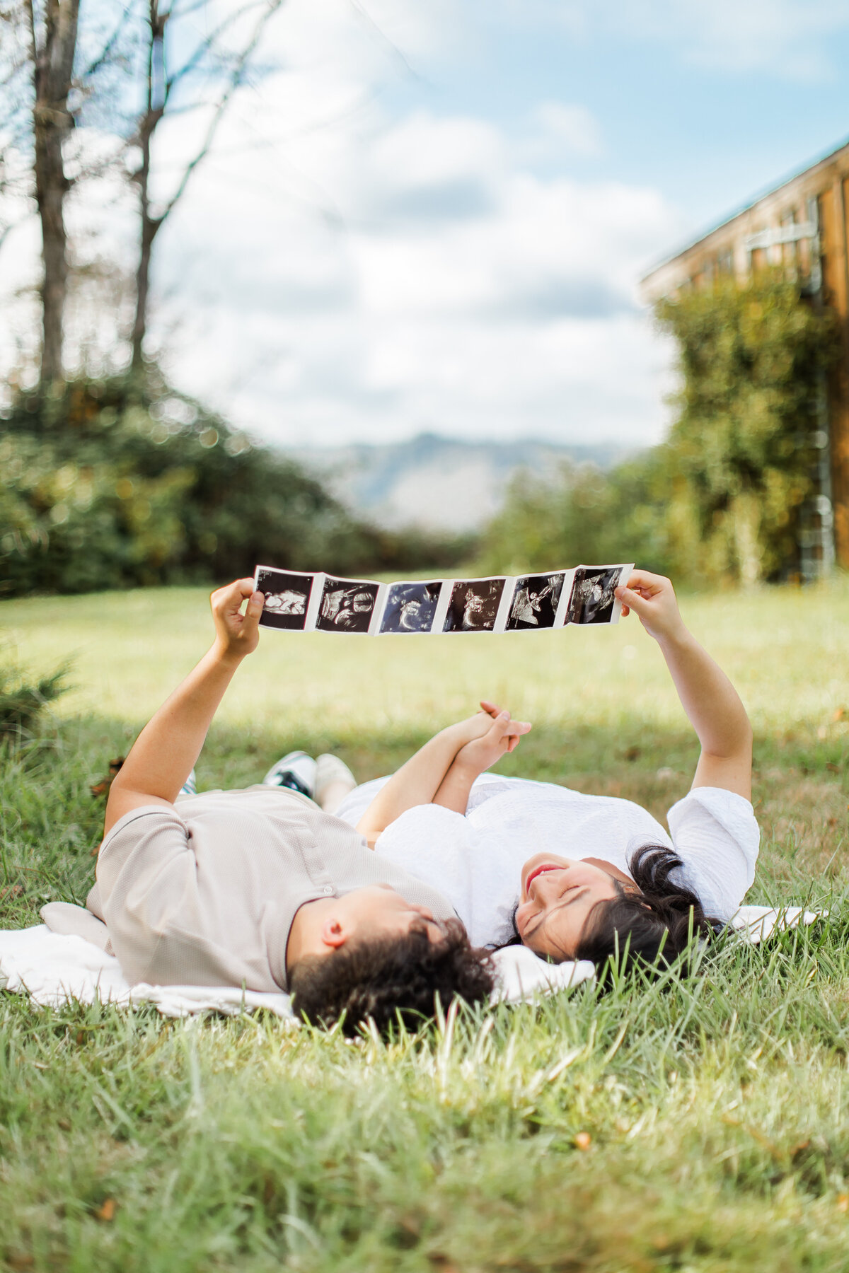 Couple lying on grass holding sonogram strip over them
