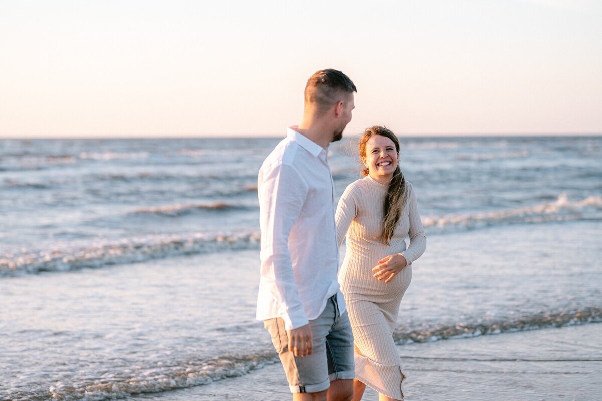 Zwanger koppel loopt langs de zee terwijl vrouw lacht naar haar maan