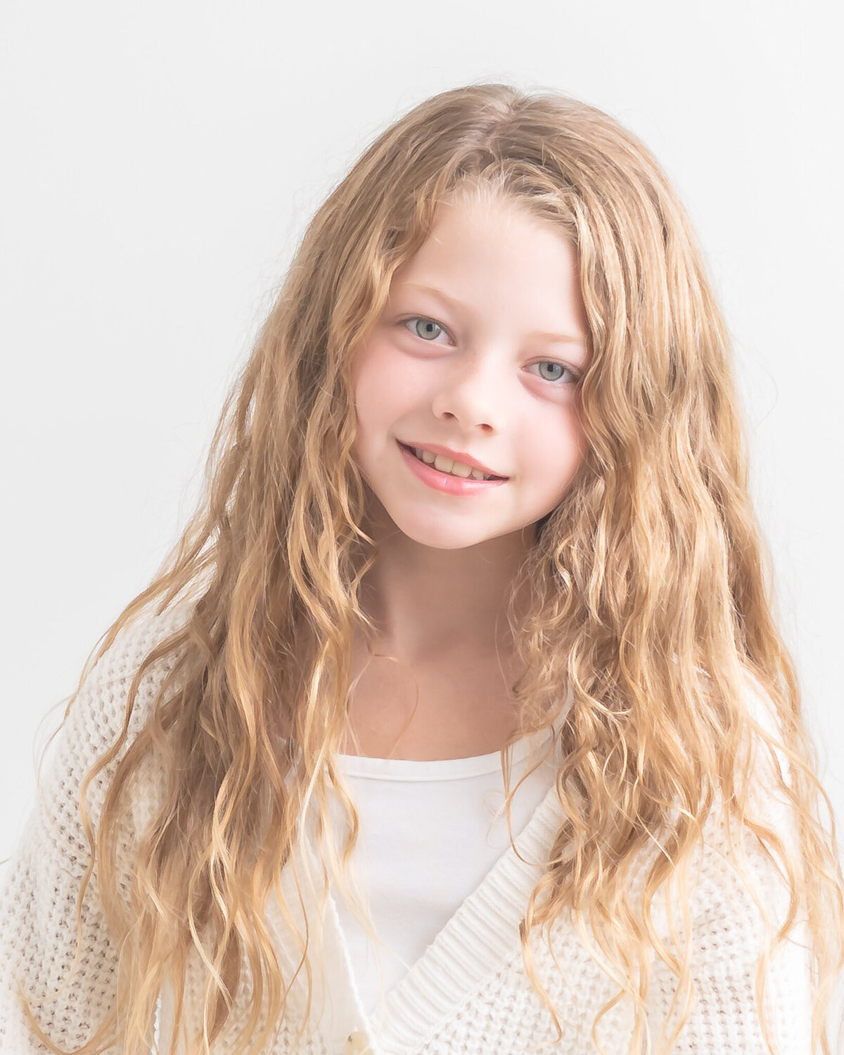 in-studio children's portrait of girl with curly blonde hair  wearing white sweater on white backdrop