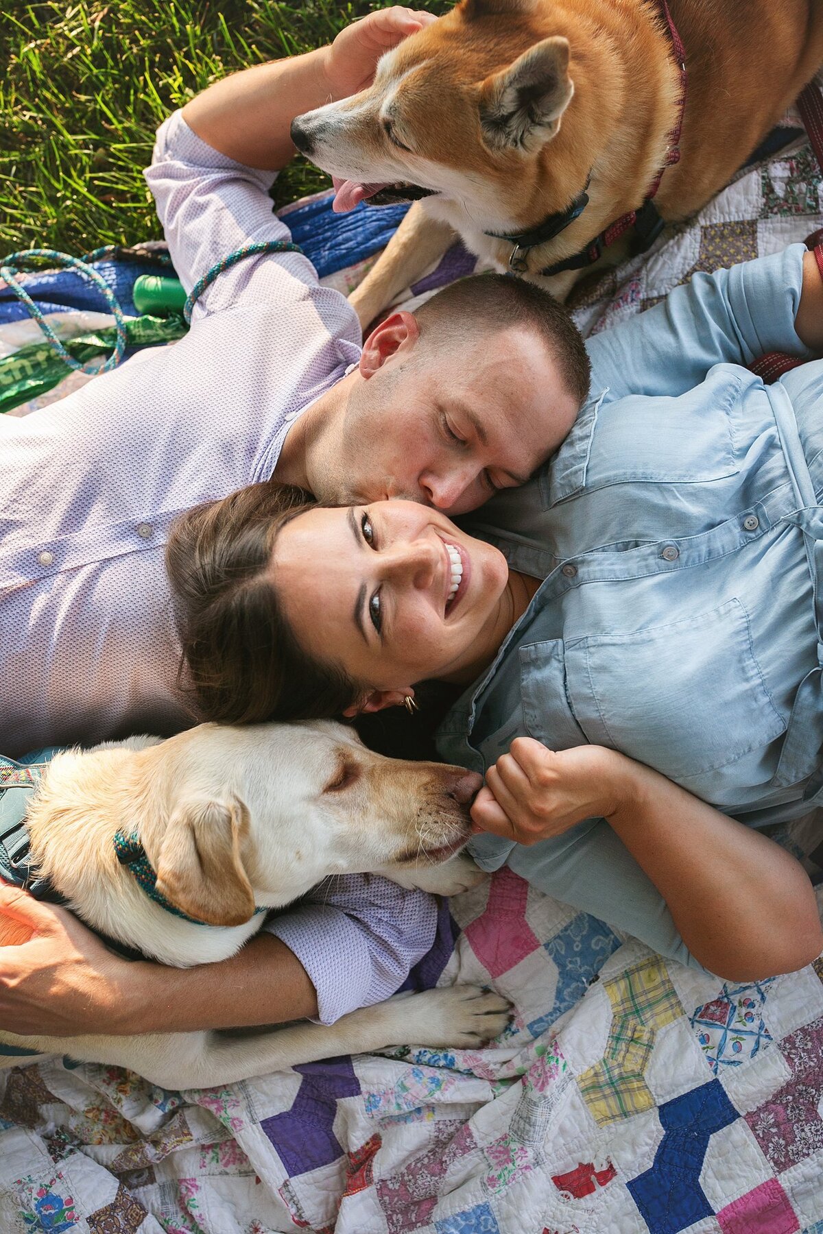 smiling-couple-with-their-two-dogs-a-labrador-and-a-shiba-inu-mix-relaxing-on-a-quilt-in-the-holy-cross-neighborhood-of-indianapolis-during-a-lifestyle-pet-and-family-session