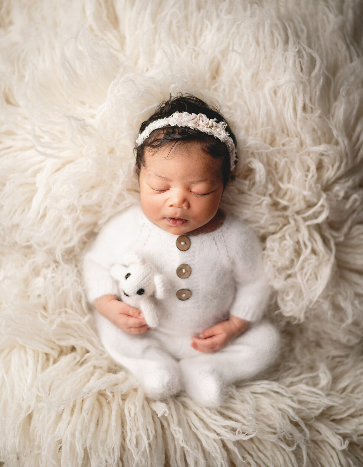 Toronto Photo Newborn girl session in white fuzzy sleeper holding a teddy on a white flokati fur.