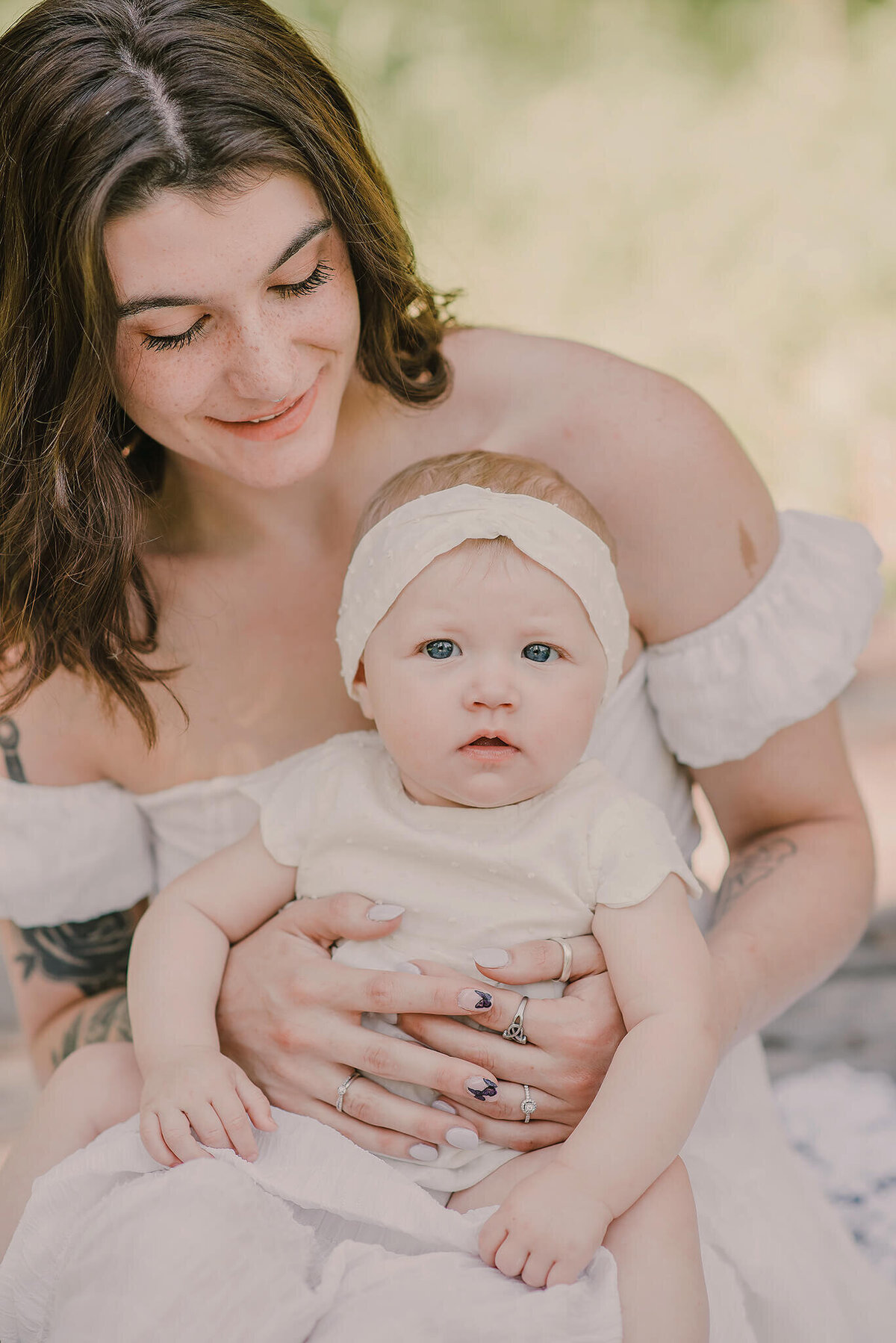An up close portrait of a mother with short brown hair holding her infant daughter on her lap. They both were white and baby girl wears a white headband. They both smile. Taken by kamloops photographer Brittany Danielle