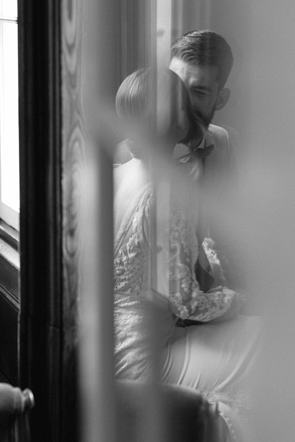 Couple de mariés qui s'embrassent derrière une porte vitrée, image en noir et blanc.