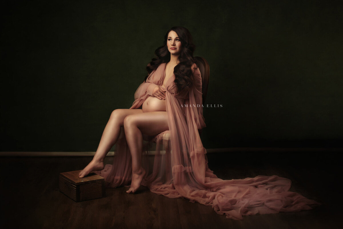 Dark and moody maternity portrait of woman posing in blush pink gown