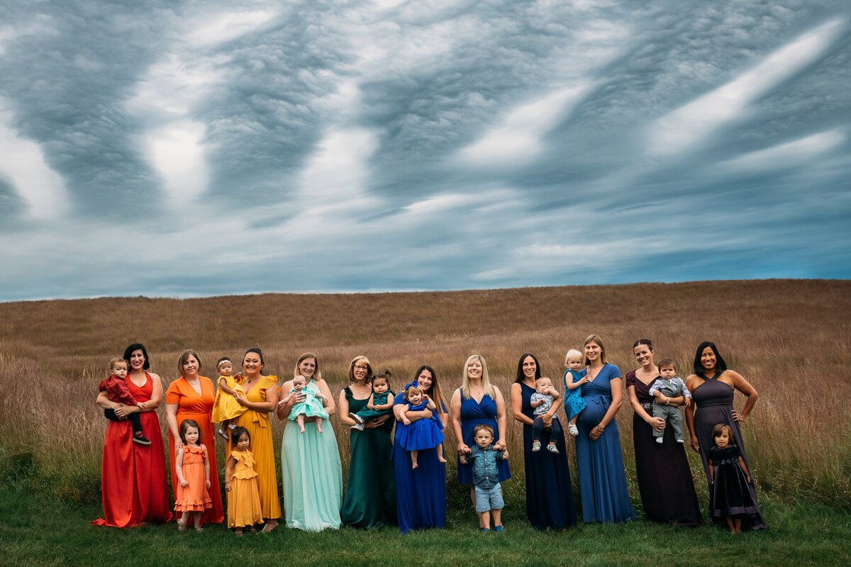 Moms & babies in rainbow dresses signifying birth after loss in wheat field with stormy skies.