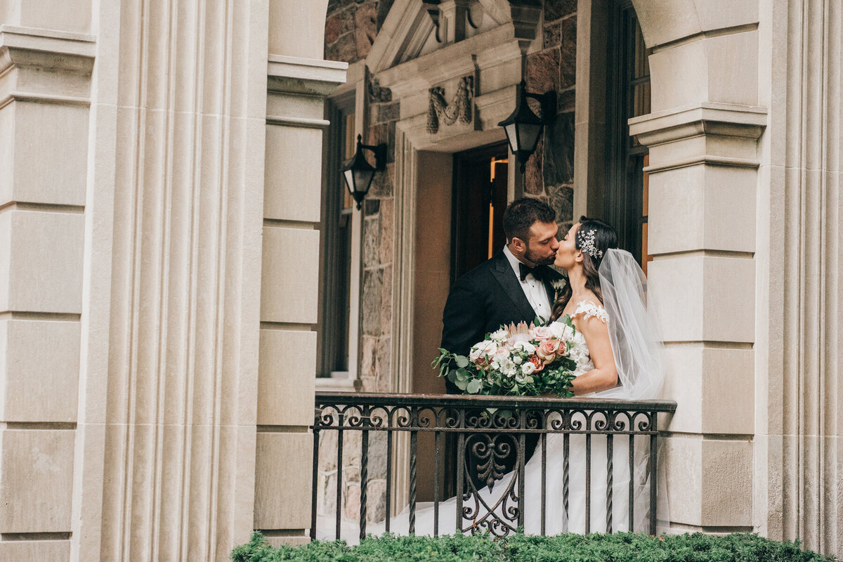 Glamorous bride and groom kiss on exquisite balcony