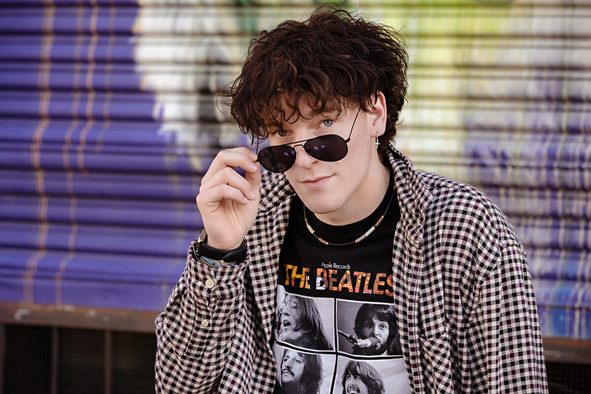 Close-up senior portrait in band tee and layered shirt, captured by Charlotte photographer in an urban industrial setting.