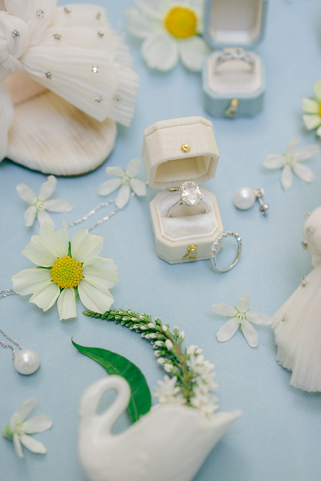 Luxury bridal detail flatlay featuring engagement ring, earrings, flowers, and ring boxes with soft blue accents at Old Edwards Inn in Highlands, NC.
