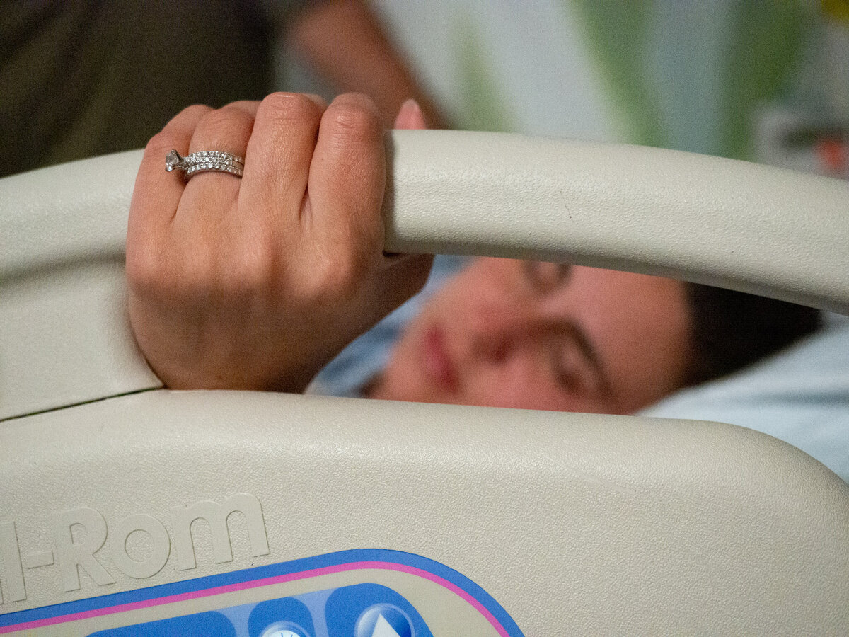 A laboring mother is holding the rail of the hospital bed, and the focus is on her wedding ring with her face in the background at a hospital in Seattle.