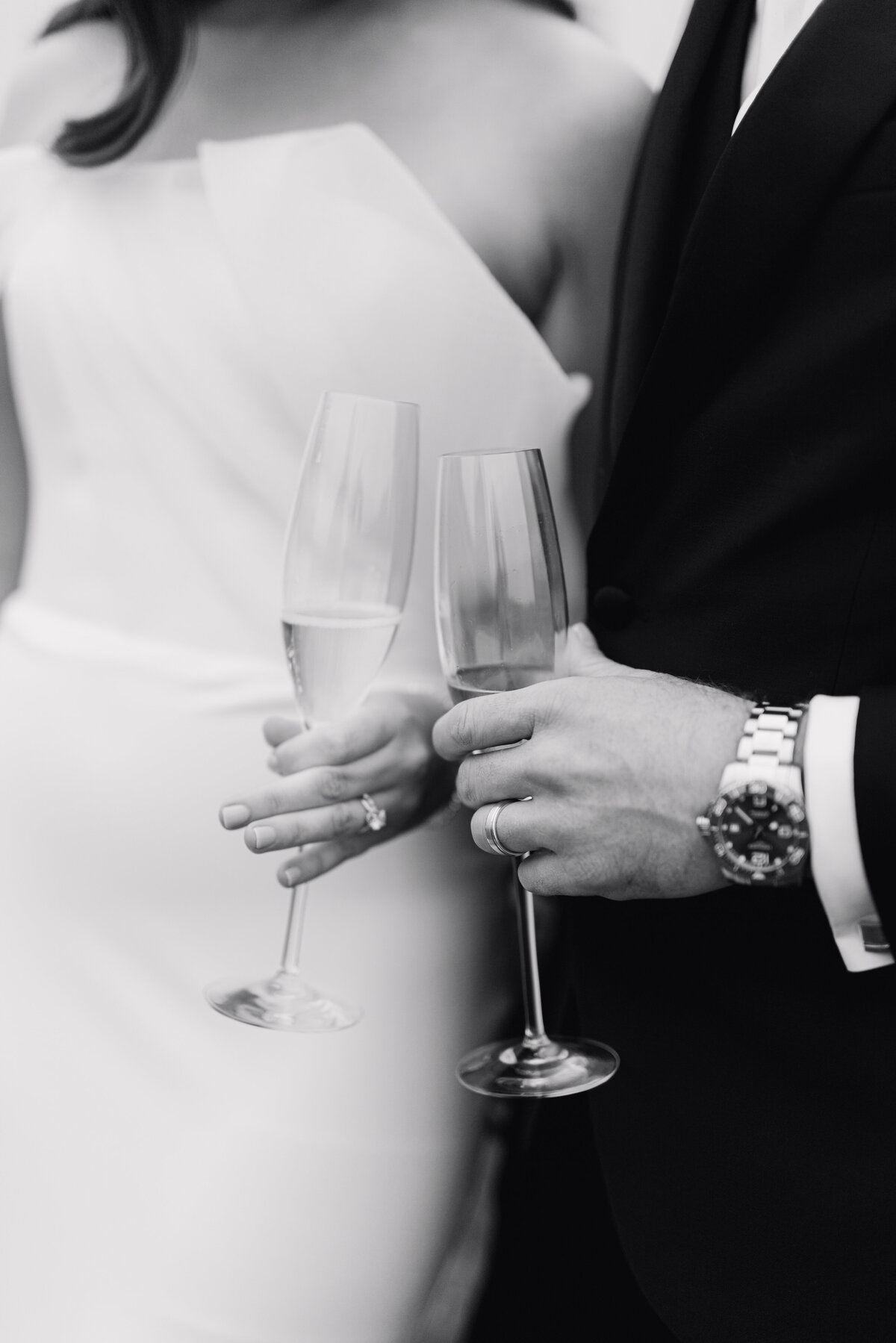 Bride and groom hold champagne glasses in black and white image by wedding photographer in Illinois Lacey Graham