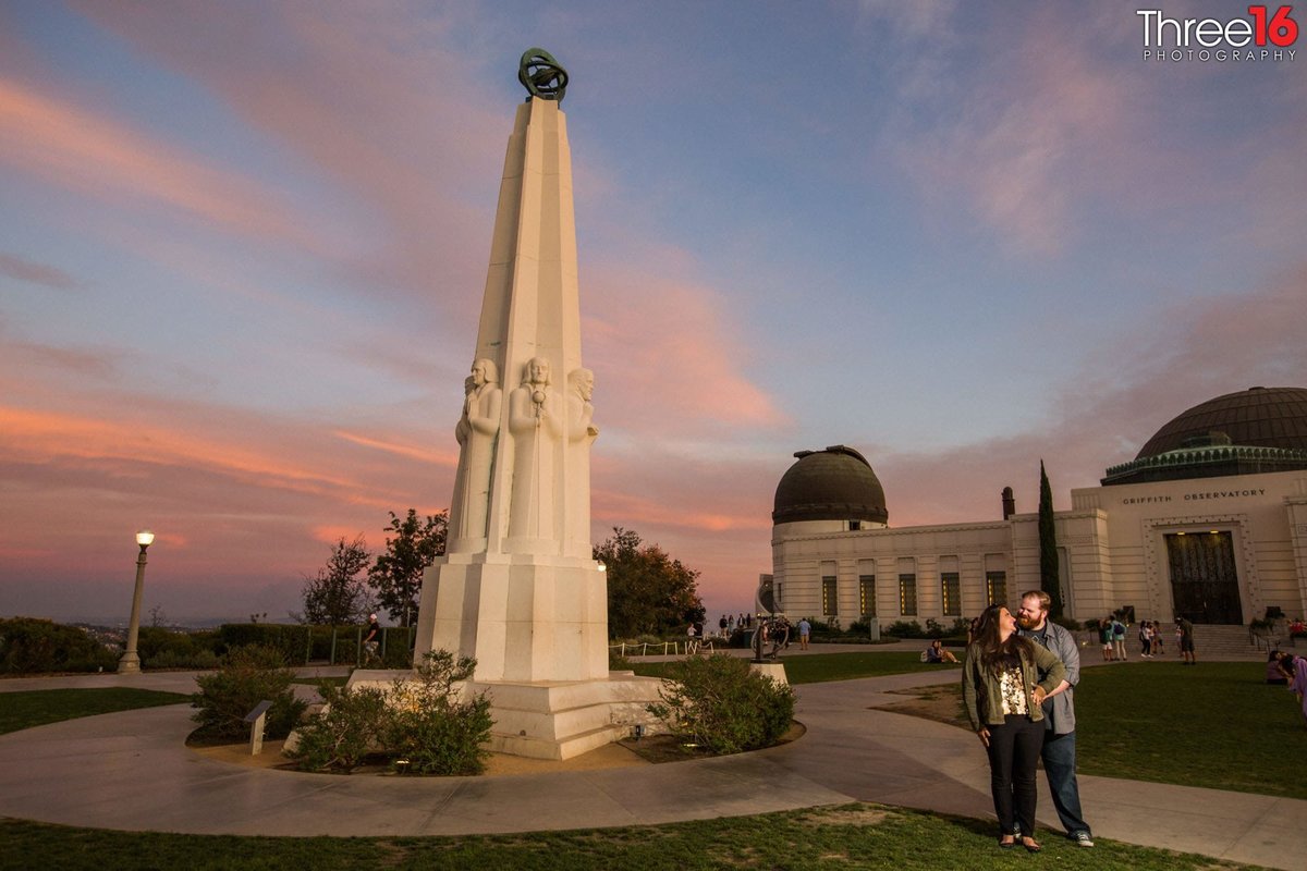 Engaged couple pose for engagement photos on the grounds of the Griffith Observatory