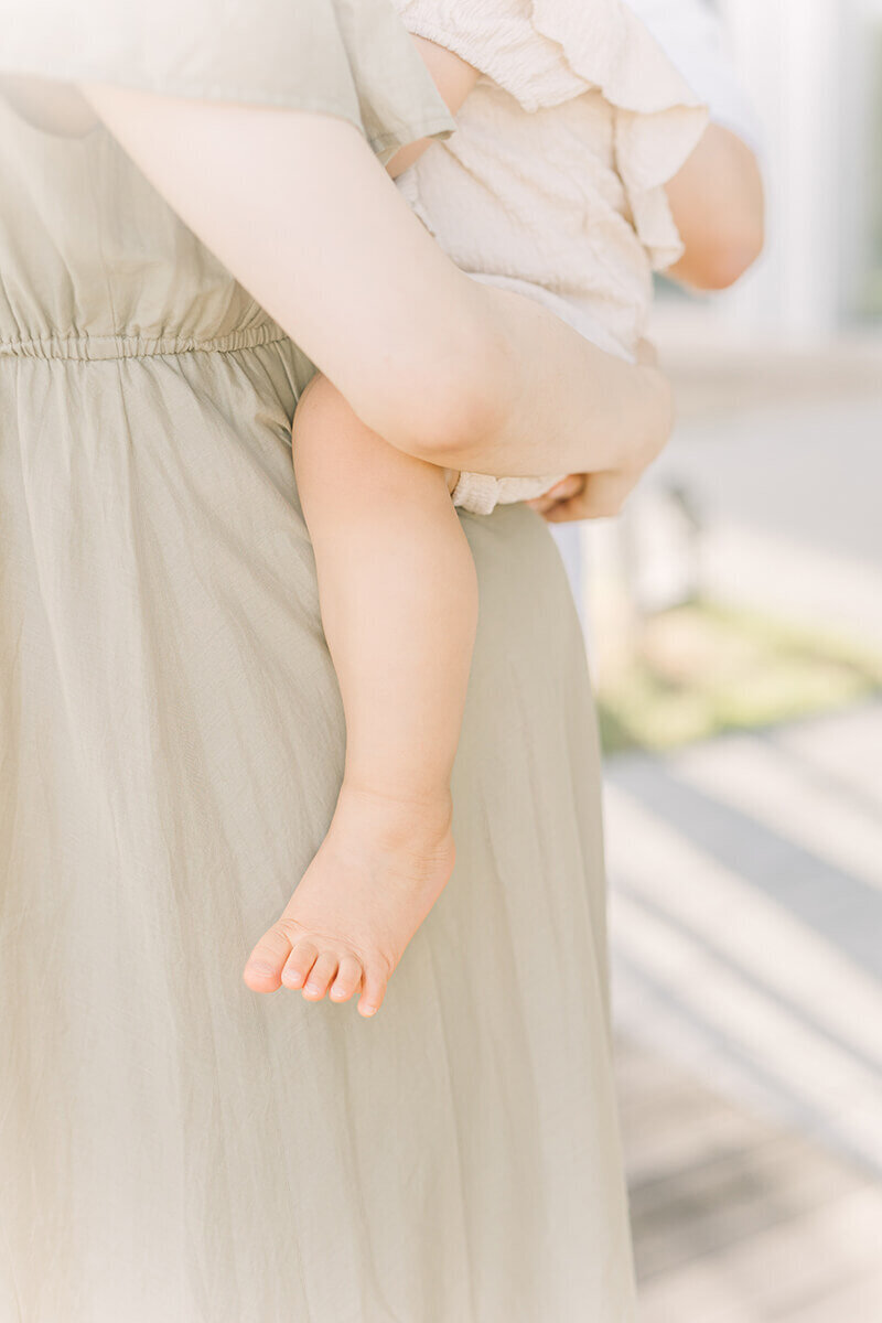 A little girl is being held by her mother on her big pregnant belly. The photograph features her little cute foot and the mother holding her tightly.
