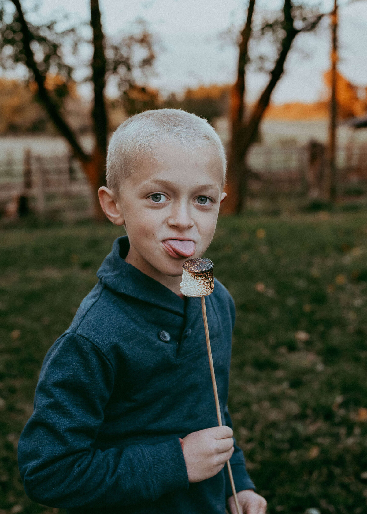 A young boy makes a silly face at the camera as he licks the marshmallow he just roasted over the fire on his families farm during a Denver family photo session.