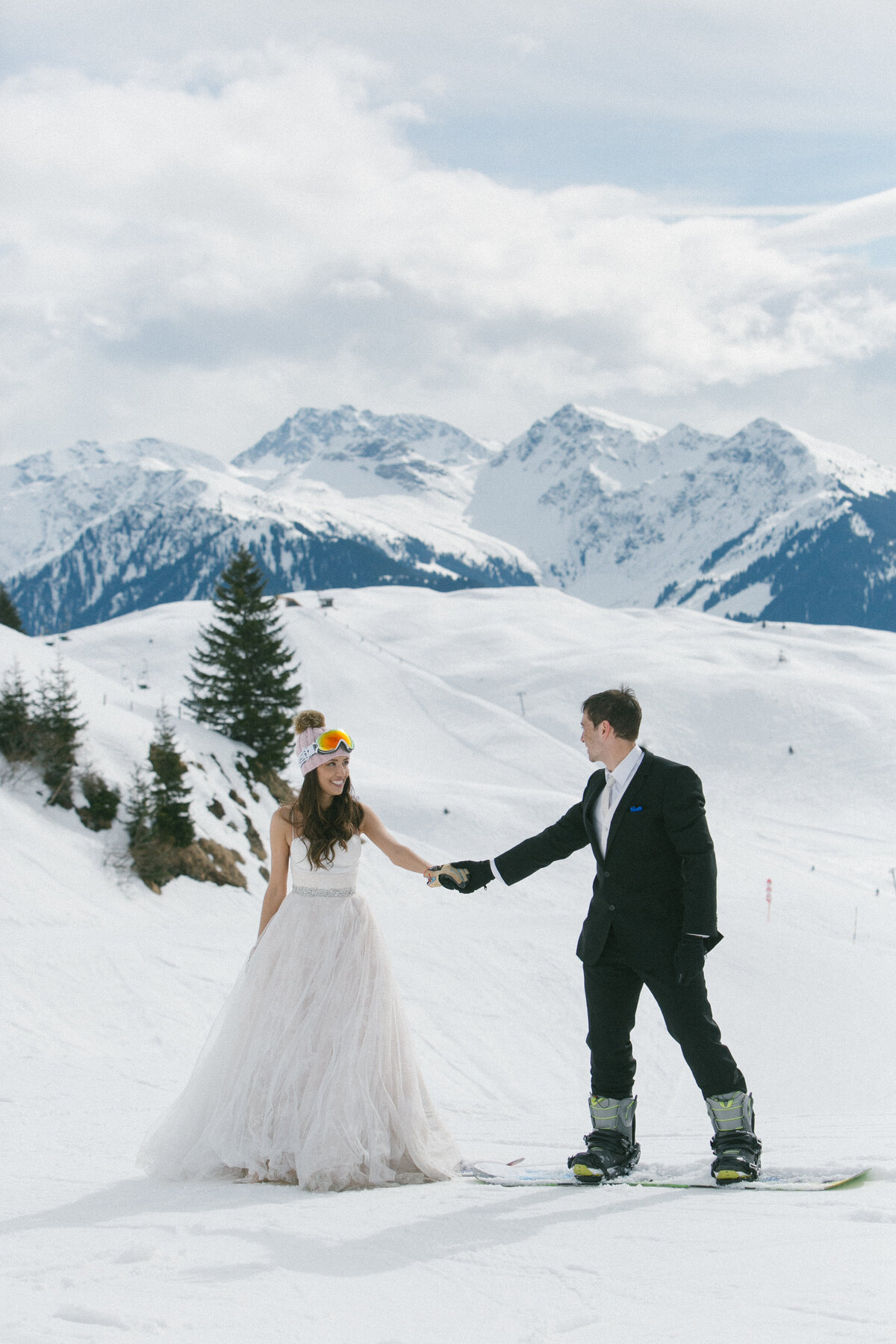 Bride, groom, and friends laughing in snow with snowboards and goggles – après-wedding energy in Kitzbühel by Studio Rose
